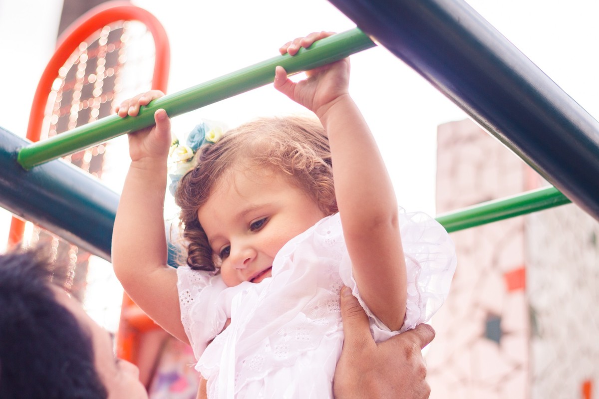 Criança brincando com o pai em um brinquedo de praça, durante ensaio família em Belo Horizonte.