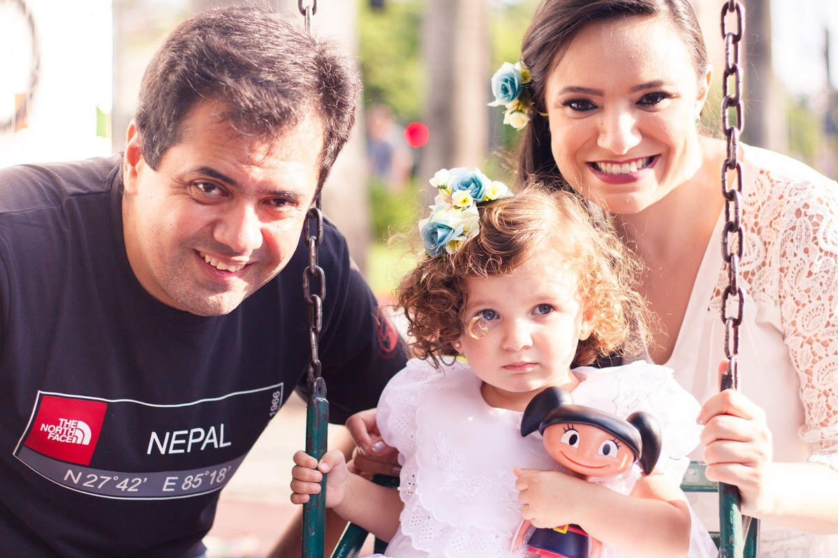 Casal com a filha de 2 anos em um balanço em praça de BH.