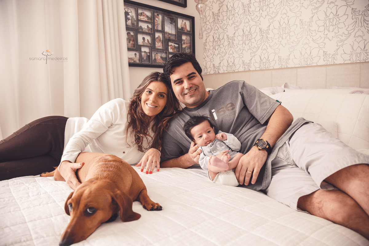 Família deitada na cama, mãe, pai, bebê recém nascido e pet, uma cachorrinha dachshund.