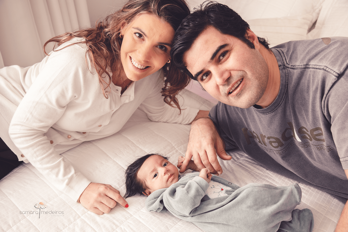 Pai, mãe e bebê recém-nascido deitados na cama e todos olhando para a foto.