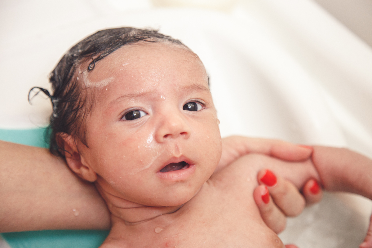 Bebê tomando banho durante seu ensaio de recém nascido, olhando para a câmera.