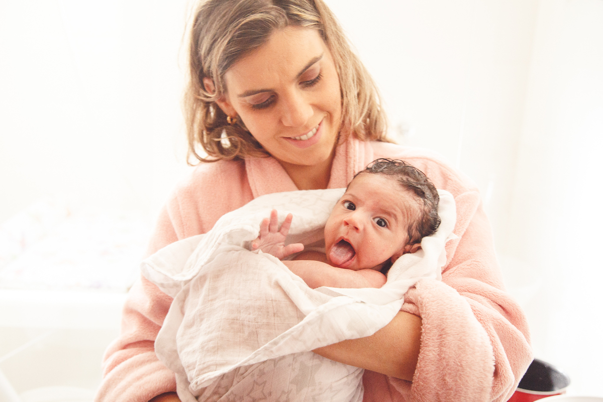 Mãe com seu bebê recém nascido, com a língua para fora, enrolado na toalha após tomar banho.