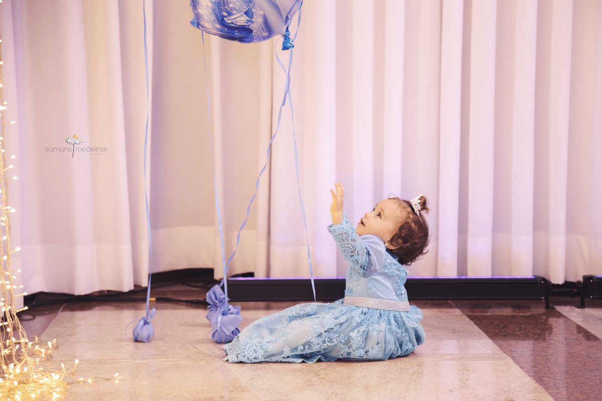 Bebê de 1 ano sentada no chão em seu aniversário, brincando com um balão no tema da festa, Cinderela.