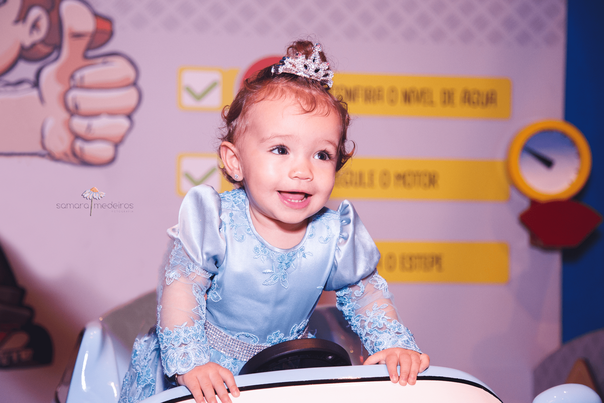 Bebê de um ano sorrindo, brincando em um carrinho, em sua festa de aniversário.