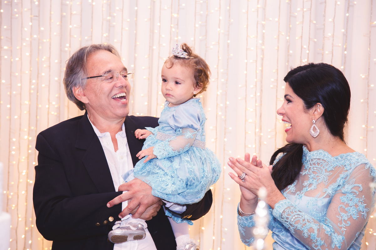 Pai, mãe e bebê de um ano durante o parabéns para você, na festa de aniversário da criança.