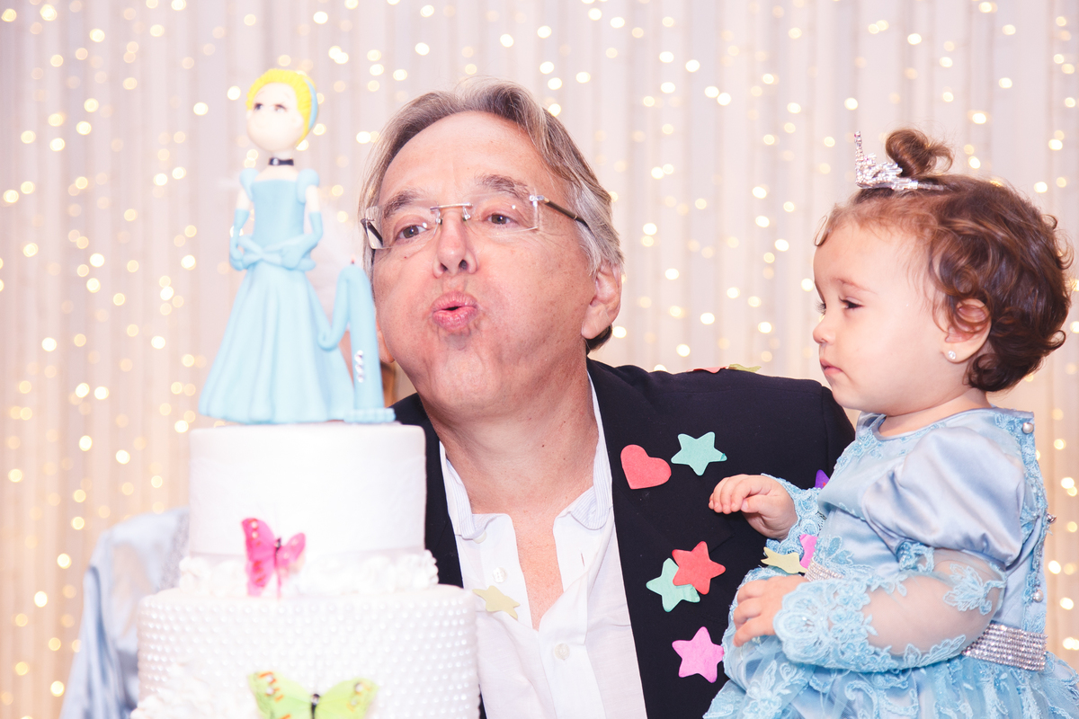 Pai e bebê soprando a vela do aniversário de um ano da menina.