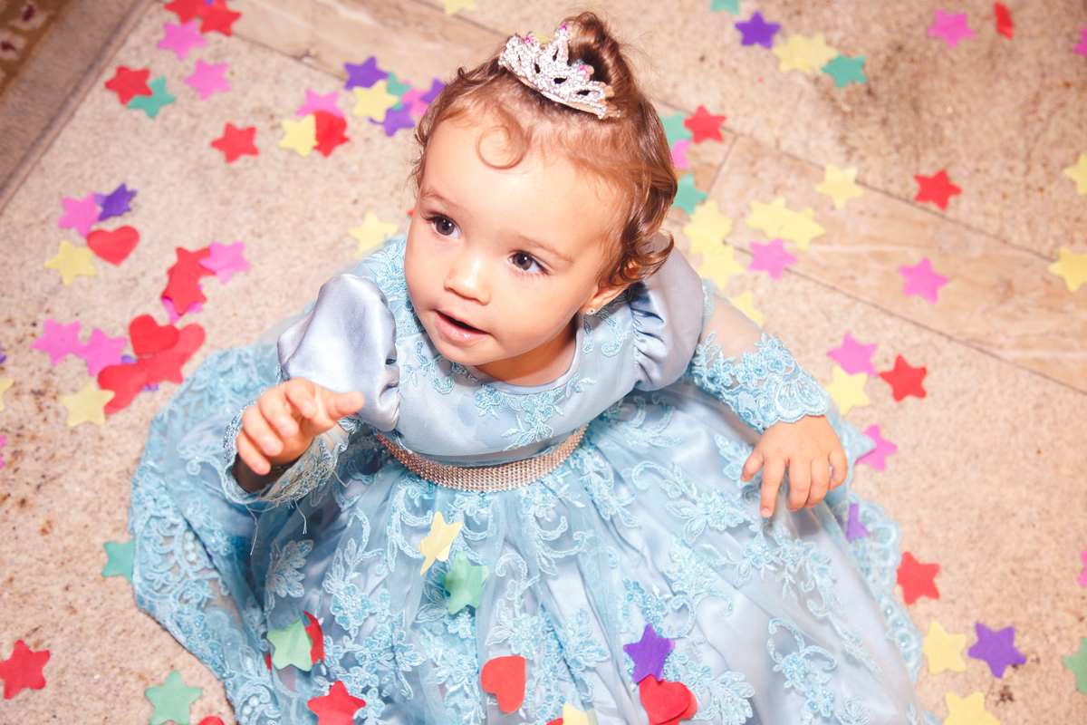 Menina de um ano no chão em sua festa de aniversário brincando com os papéis picados que caíram após o parabéns.