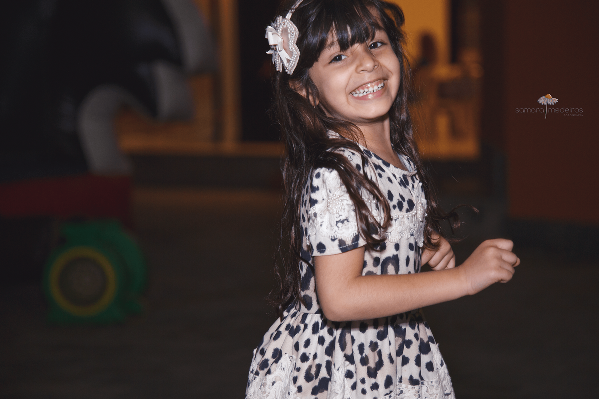 Criança correndo em uma festa de aniversário infantil, ao mesmo tempo que sorri e posa para a foto.