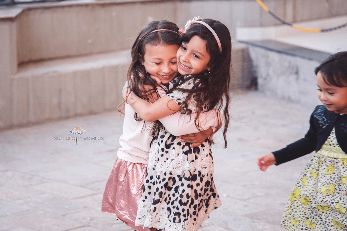 Duas crianças se abraçando e sorrindo, uma delas com os olhos fechados, em festa de aniversário.