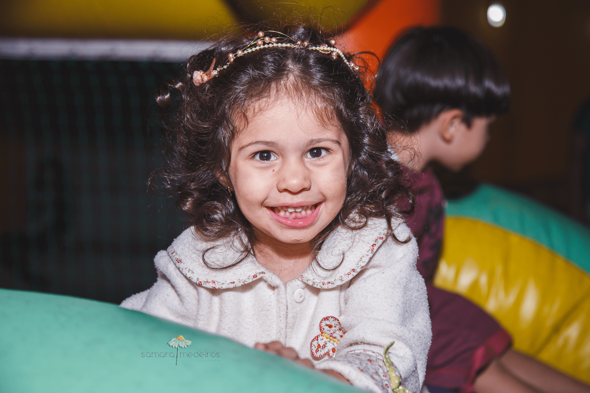 Criança em cima de um brinquedo inflável, olhando para a câmera e sorrindo.
