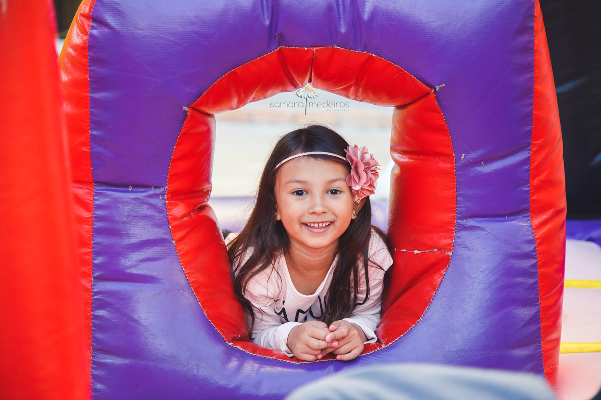 Criança de 6 anos em sua festa de aniversário brincando no brinquedo inflável e posando para foto, com um sorriso.