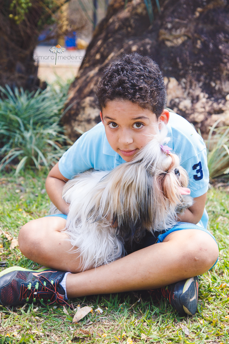 Uma criança com a cachorrinha shih-tzu no colo, enquanto a criança olha para a foto, a cachorra olha para o lado.