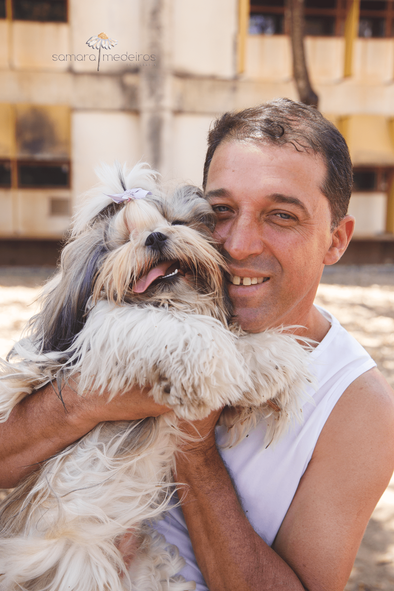 Shih tzu com seu tutor, sendo abraçada com uma expressão de sorriso e a língua para fora.