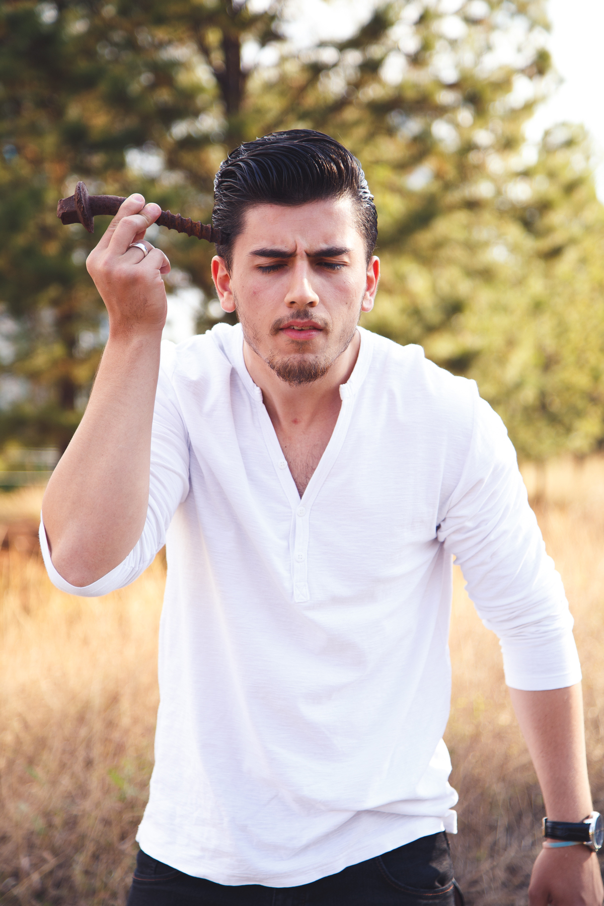 Rapaz com um parafuso enorme na mão fingindo que está encaixando na própria cabeça, com uma expressão curiosa.