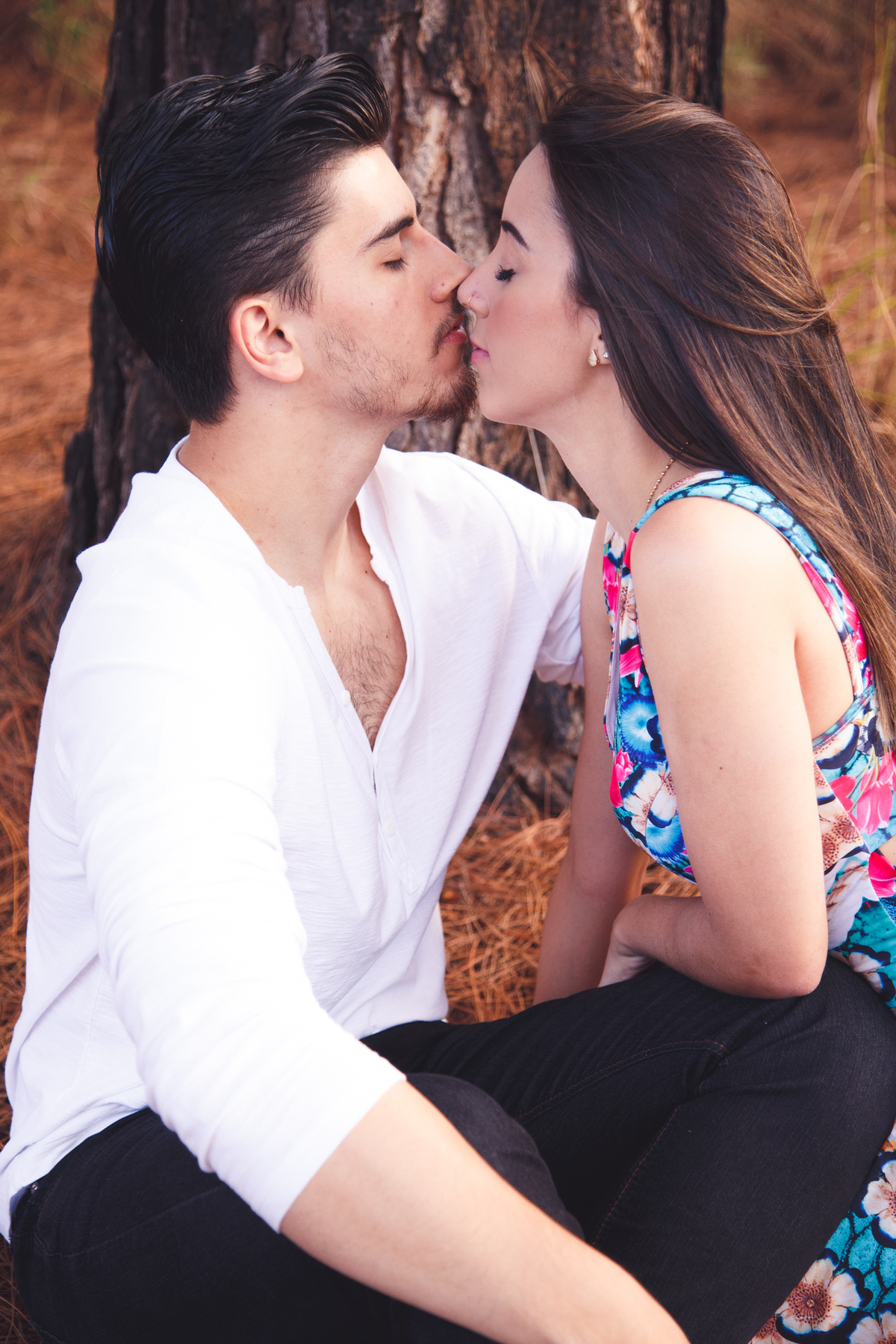 Casal sentado em um tapete de folhas caídas, se olhando, prestes a se beijar.