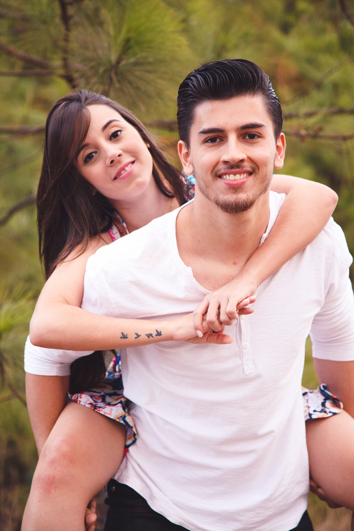 Casal brincando durante sessão fotográfica. A moça nas costas do rapaz, o abraçando por trás e ambos sorrindo.