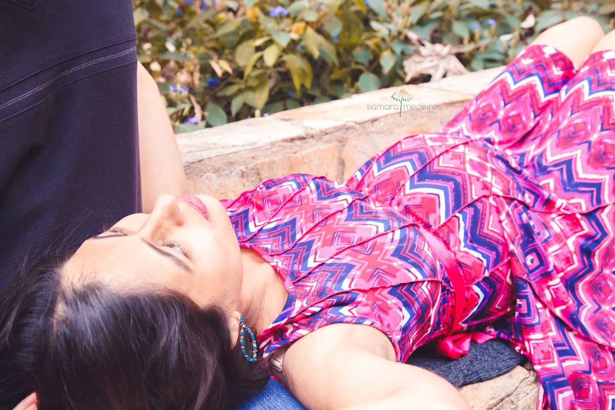 Gestante deitada no colo do marido, olhando para ele com expressão pensativa.