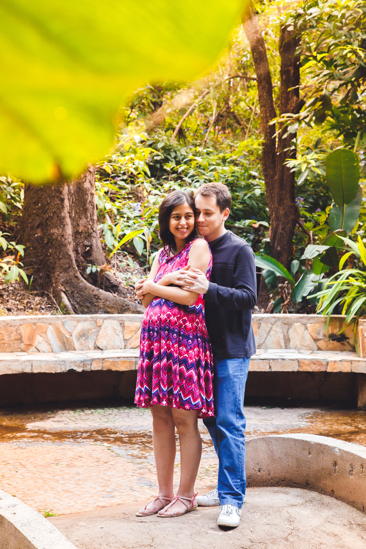 Mulher grávida e pai abraçados de mãos dadas sorrindo.