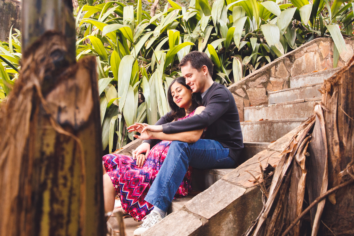 Marido e esposa sentados em uma escadaria de pedra observando as próprias mãos e sorrindo.