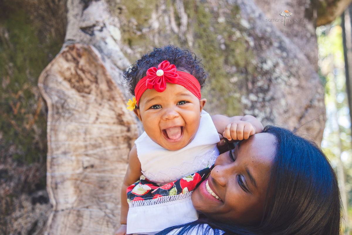 Mãe e filha brincando durante sessão de fotos em Belo Horizonte. A mãe joga a bebê para cima, que gargalha.