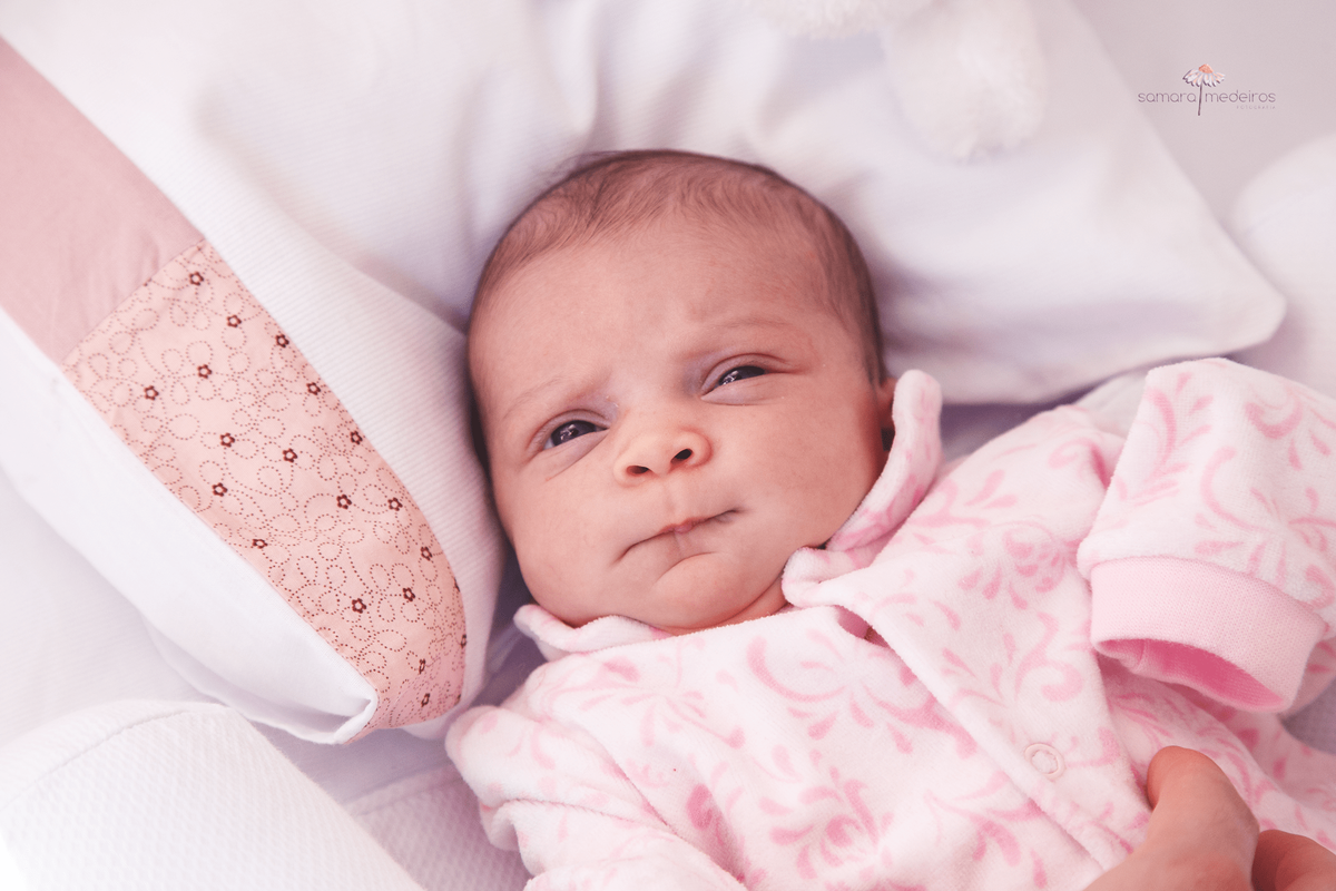 Bebê recém nascida deitada em seu berço fazendo careta.