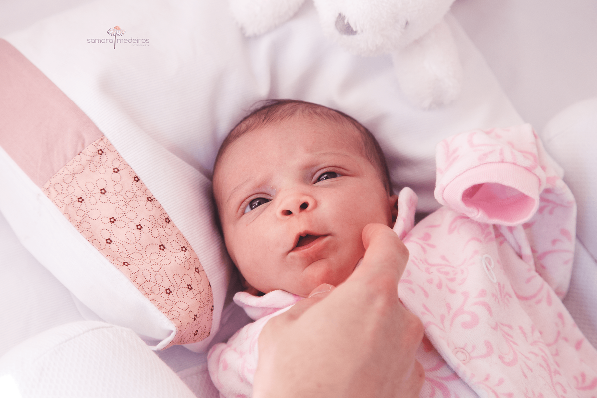 Bebê de 19 dias deitada em seu berço e fazendo careta enquanto seu pai faz cócegas em seu rosto.