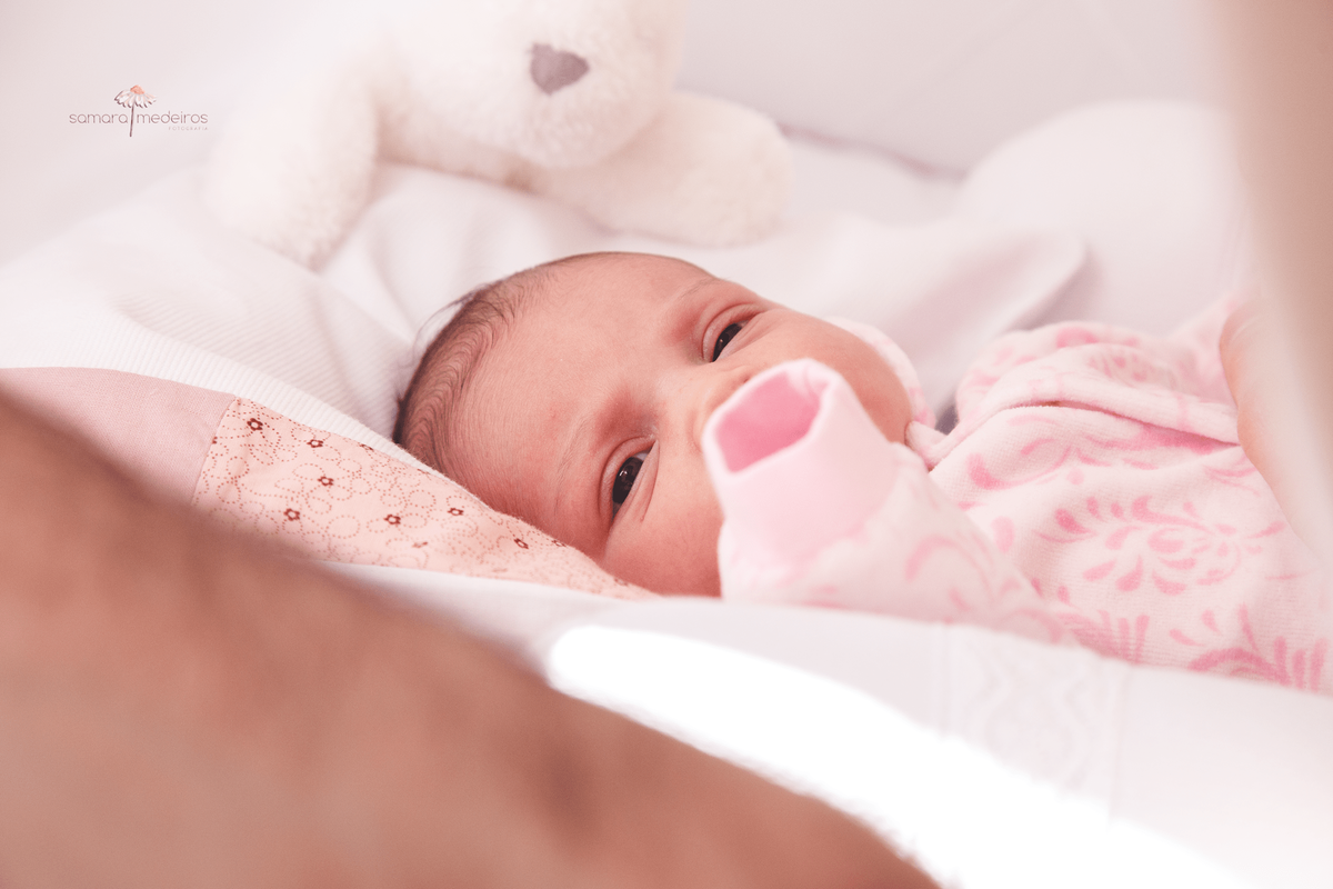Bebê recém nascida deitada em seu berço observando o pai, que também a observa.