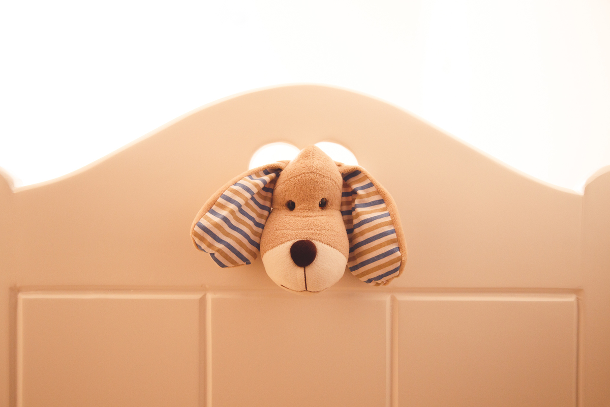Detalhe do berço com a cabeça de um cachorro de pelúcia passando por uma abertura em formato de coração na face do berço.