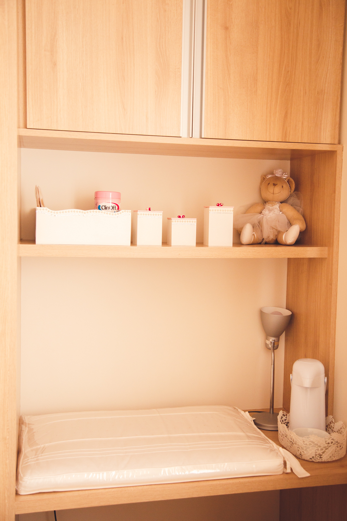 Detalhes de enfeite em uma prateleira no quarto da bebê, com potes de algodão, cotonetes e um urso de pelúcia.