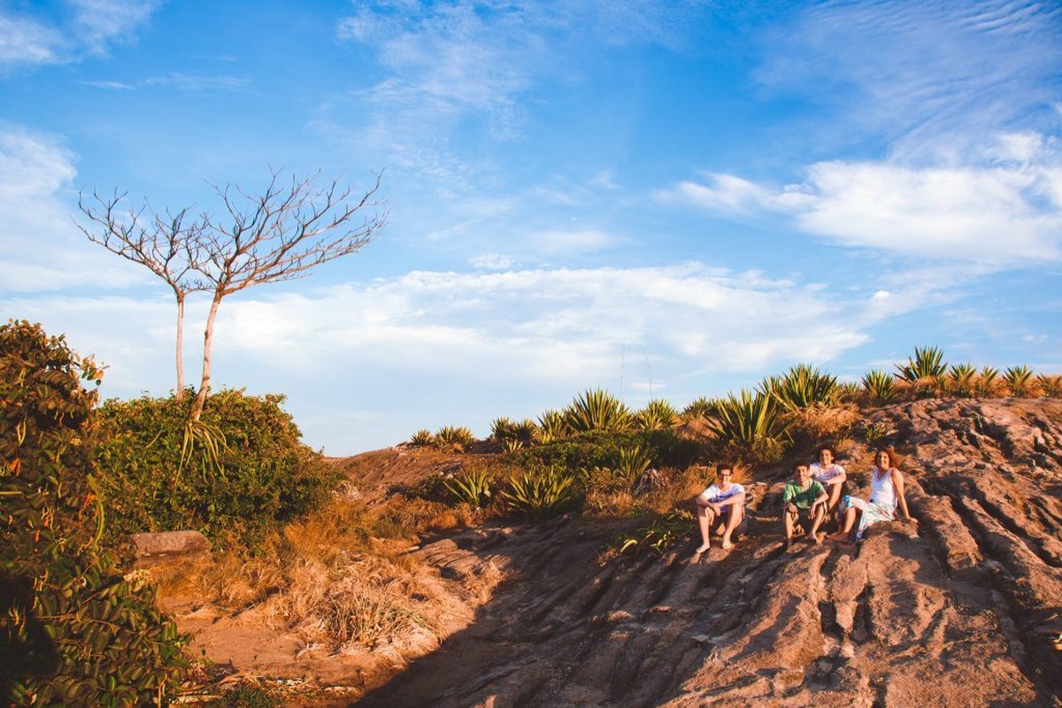 Foto panorâmica nas montanhas de Vitória, próximo ao mar, com uma mãe e seus três filhos adultos sentados.