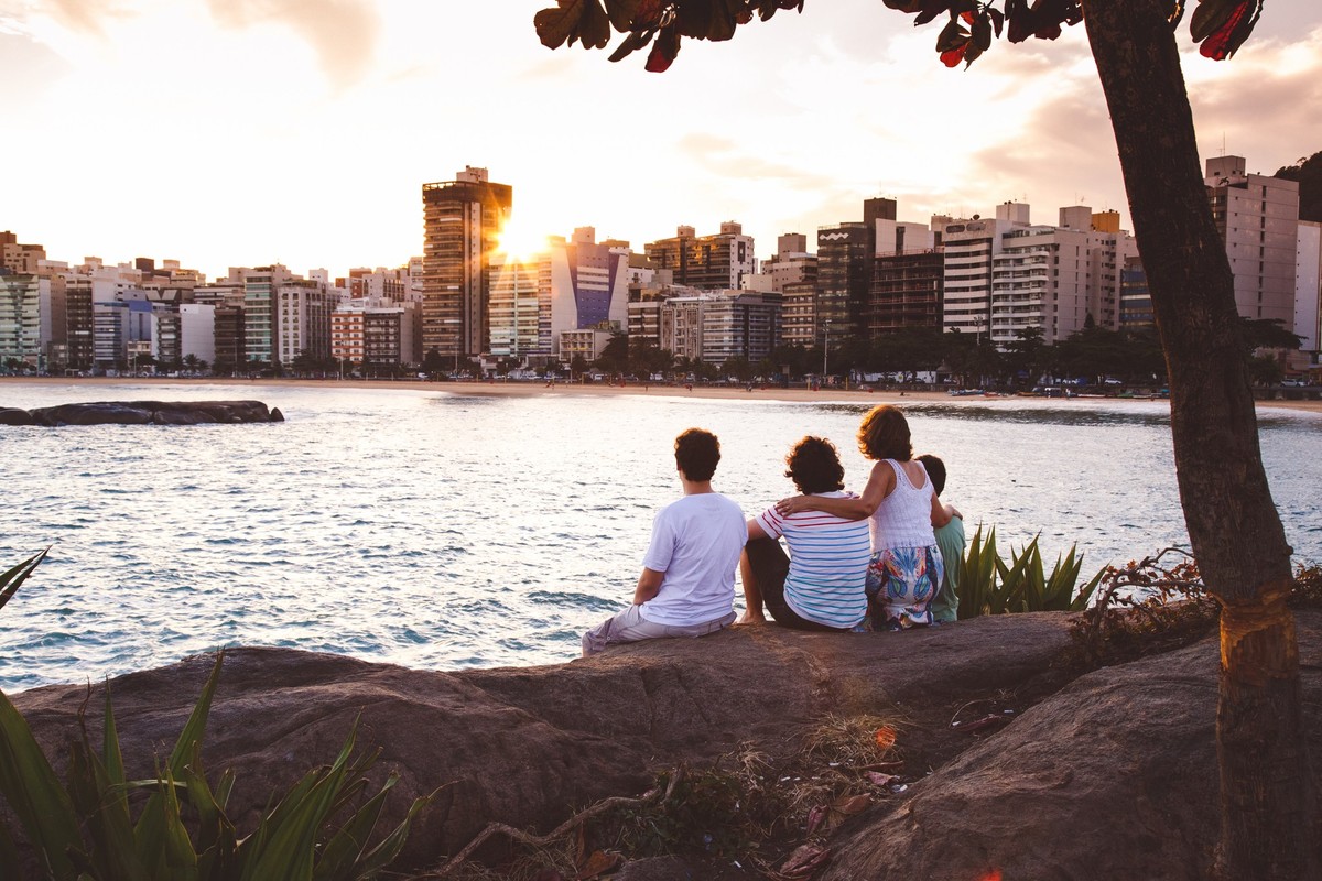 Mãe e seus três filhos adultos sentados nas pedras de uma pequena ilha na praia de Vitória, 