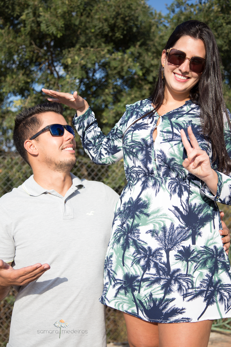 Moça em cima de um banco mostrando que está mais alta que o namorado e fazendo gracinhas. Ambos sorrindo.