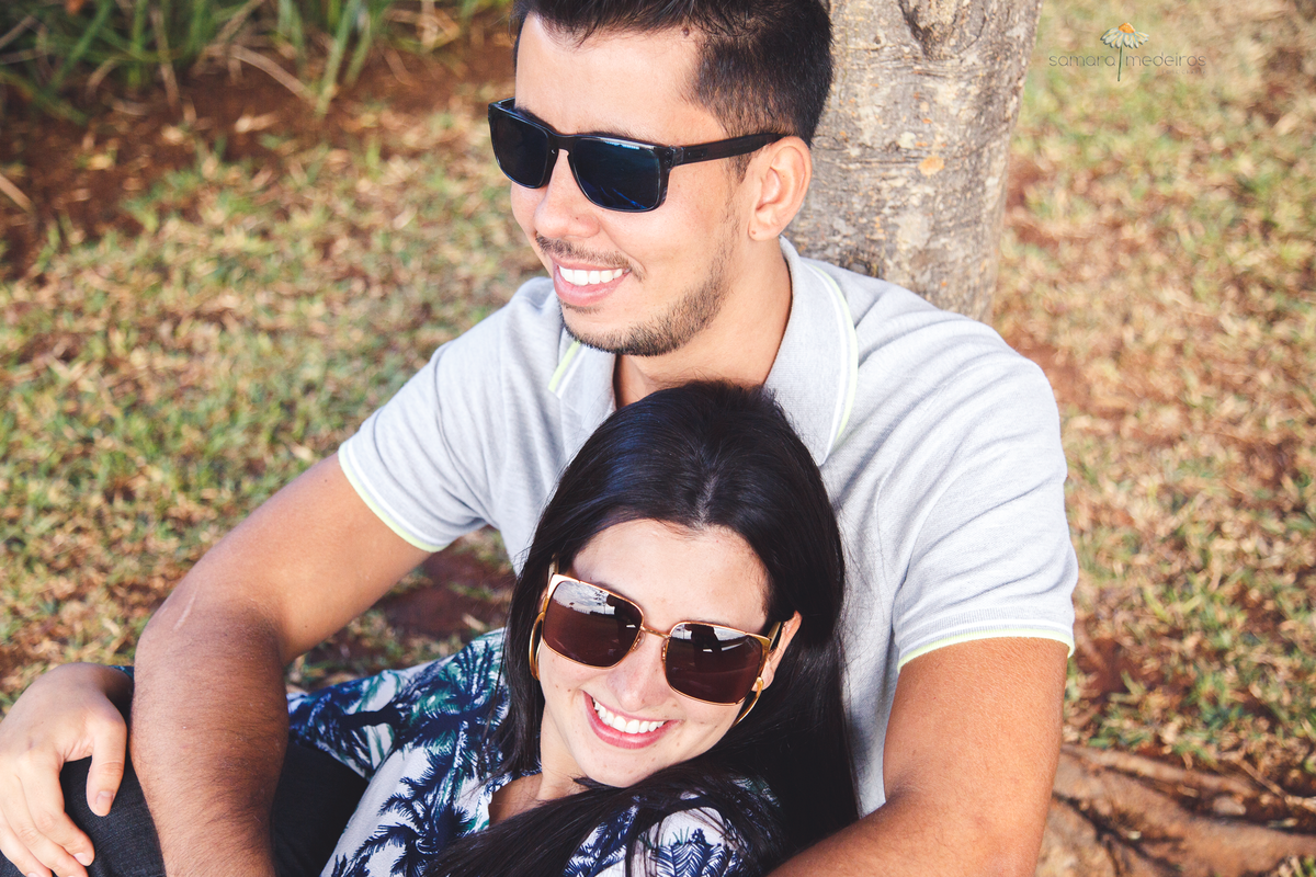 Casal abraçado, sentados recostados em uma árvore aproveitando a sombra e o momento juntos.