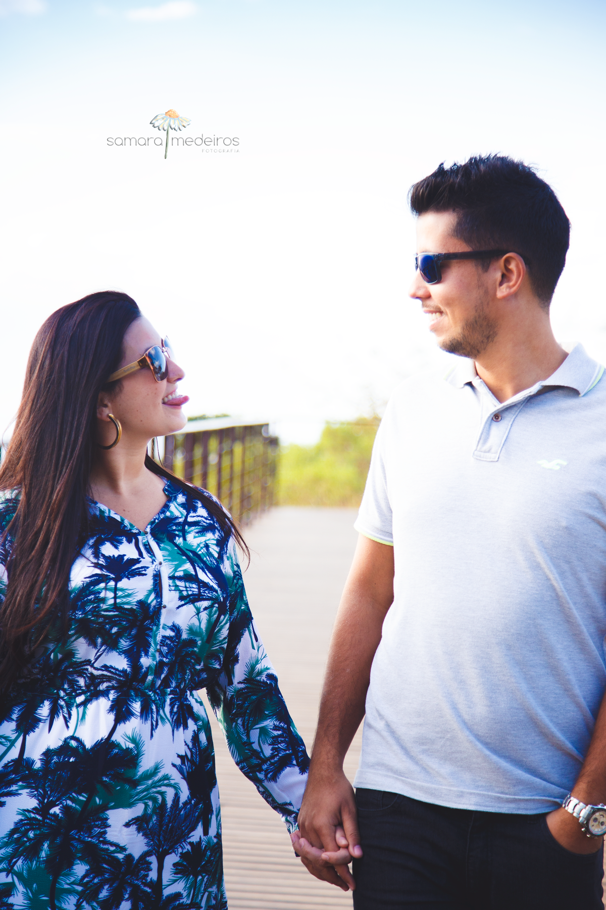 Casal andando de mãos dadas, curtindo o momento, fazendo gracinhas um para o outro, durante o ensaio fotográfico de casal.