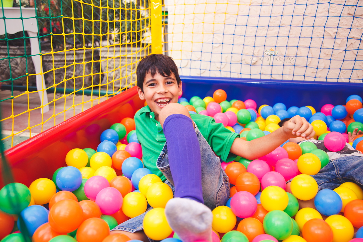 Criança de 8 anos brincando na piscina de bolinhas, desequilibrando e rindo muito.