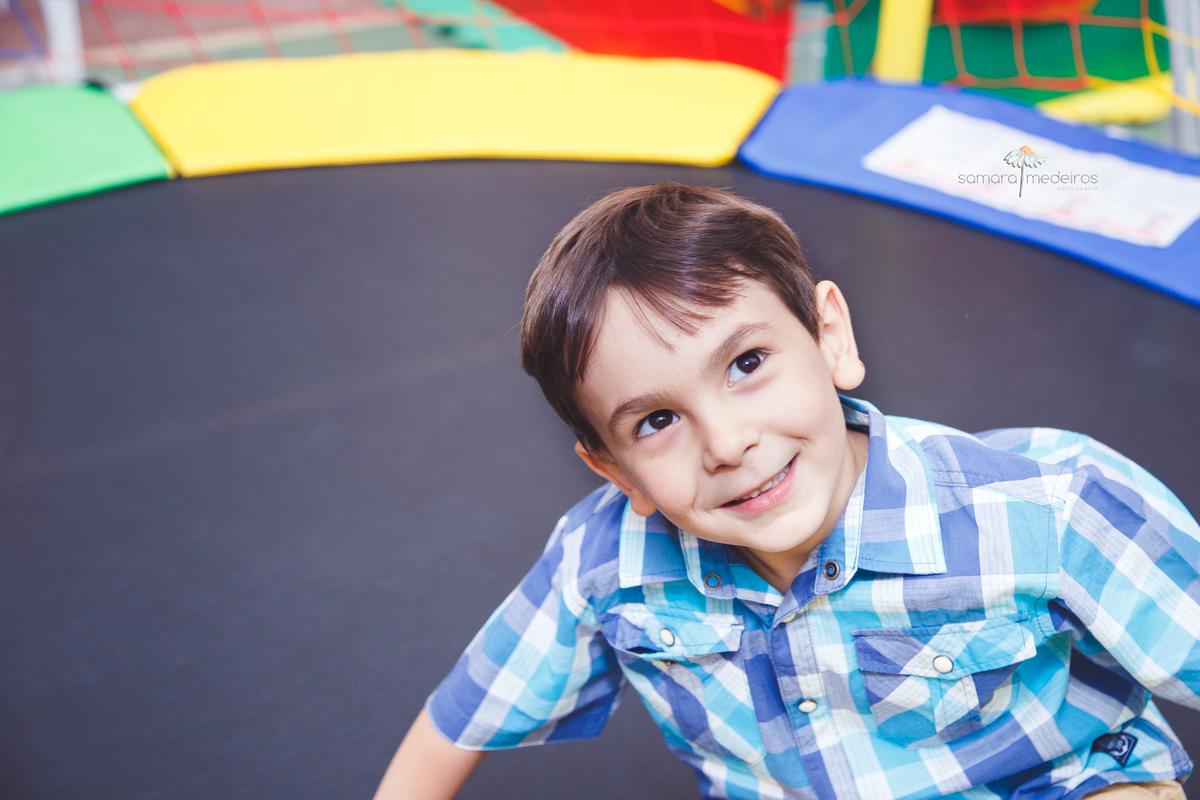 Criança brincando na cama elástica, sentada e sorrindo para alguém.