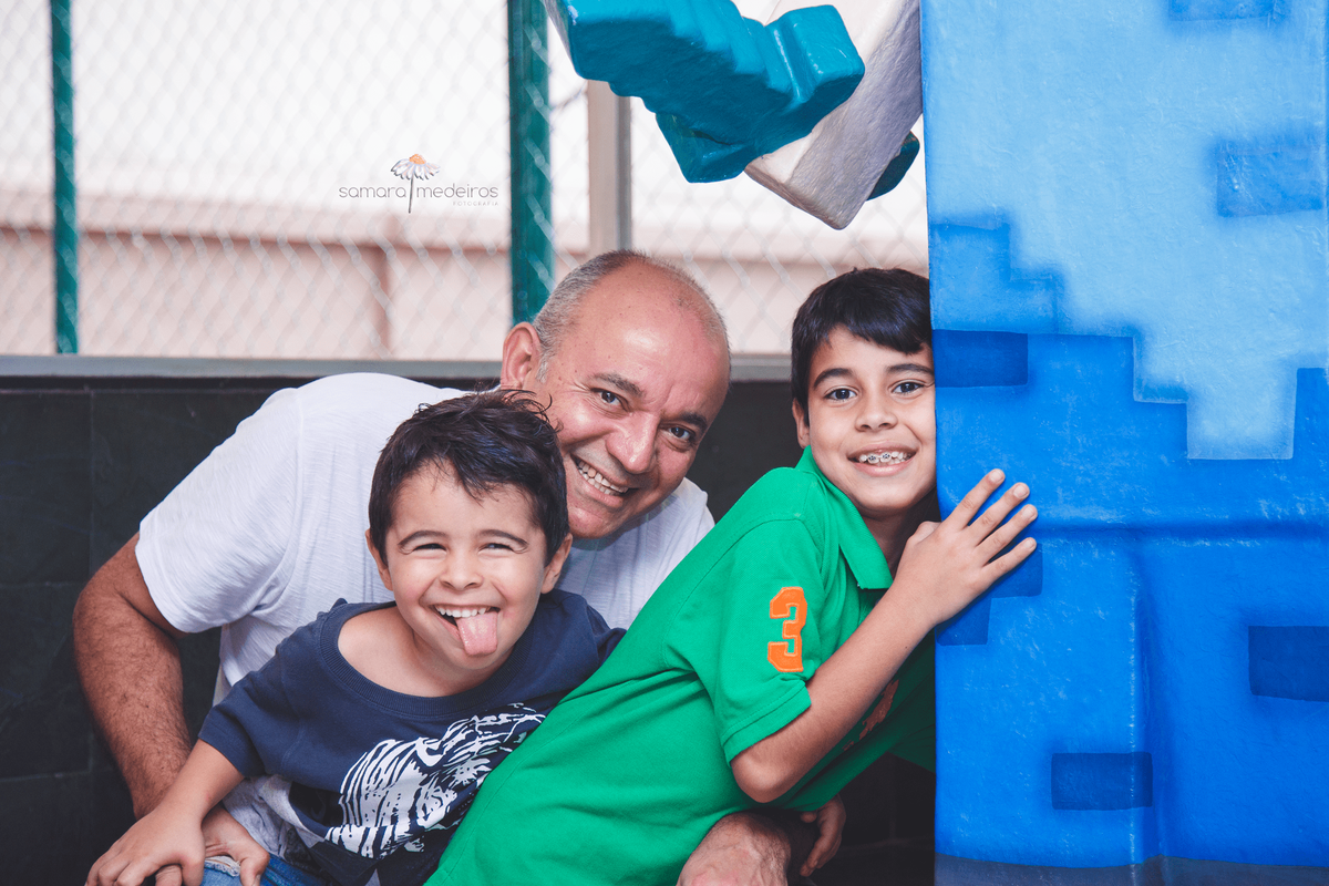 Duas crianças, de 4 e 8 anos, com seu pai posando para foto, sorrindo e fazendo careta.