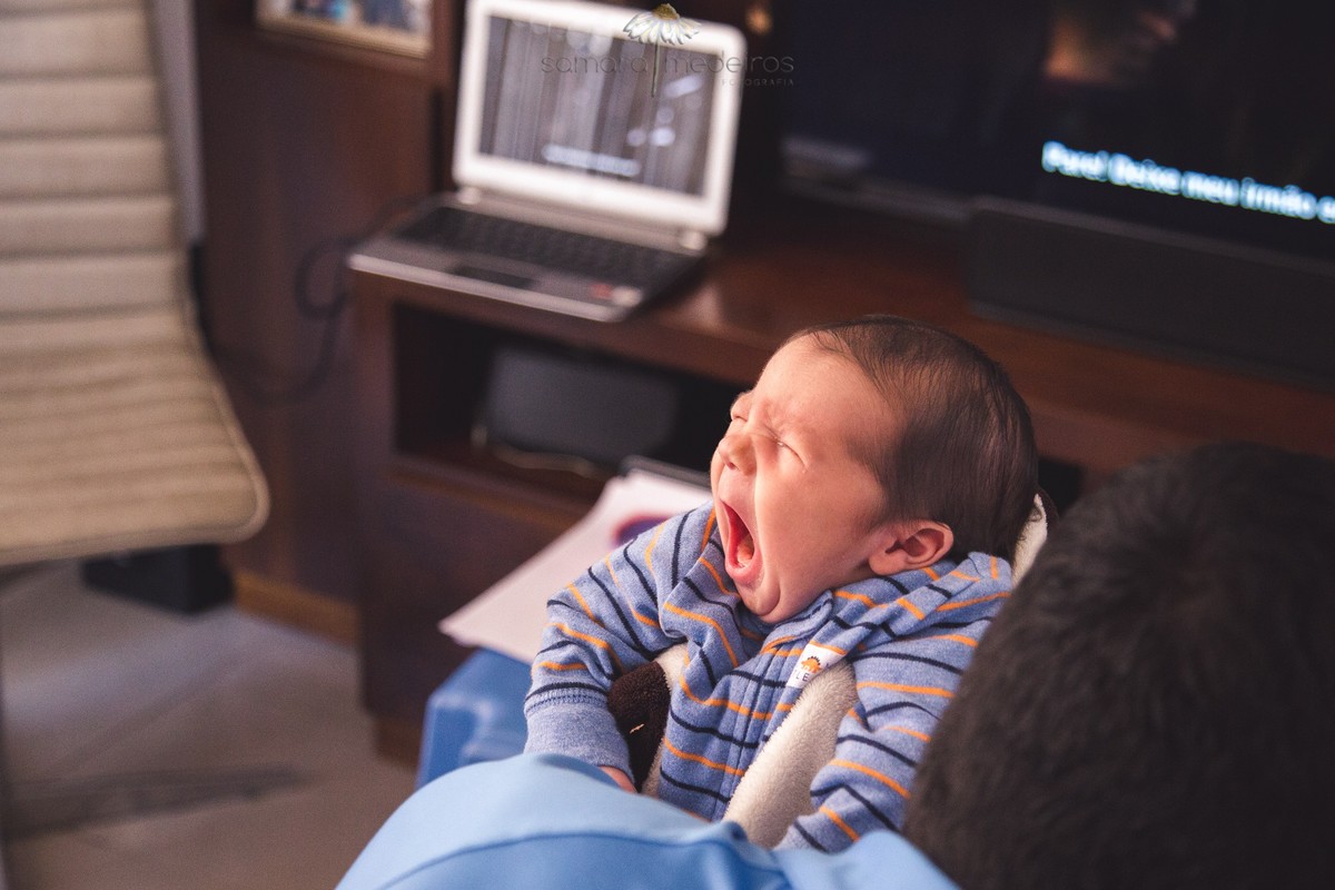 Bebê no colo do pai dando um bocejo, no início da sessão newborn, em Belo Horizonte.