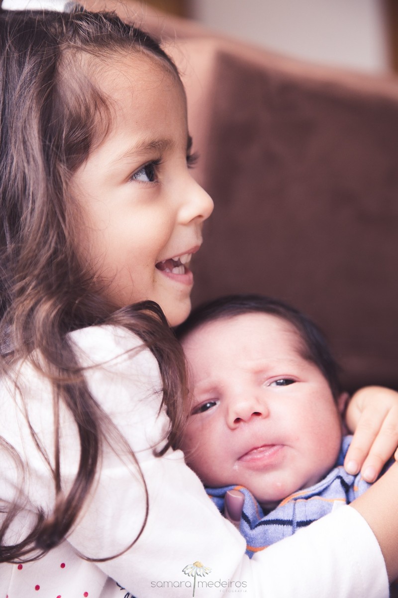Criança mais velha segurando o irmão mais novo com 15 dias de vida, durante ensaio fotográfico de família.