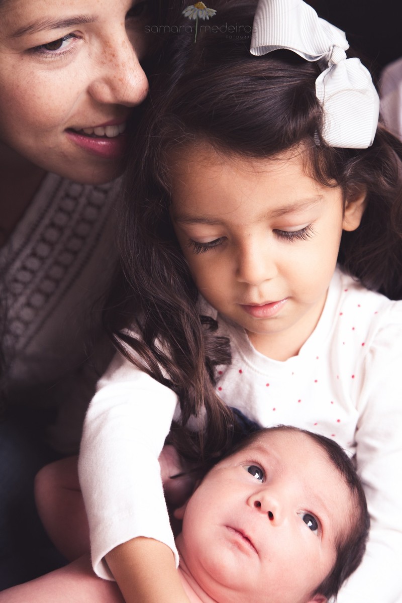 Irmã mais velha segurando no colo o irmão recém-nascido em sessão newborn lifestyle, em Belo Horizonte.