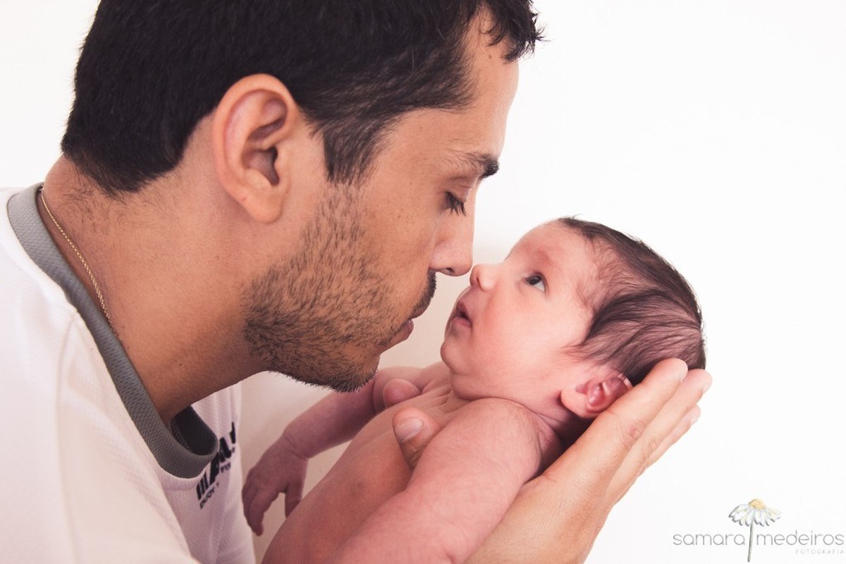 Pai segurando bebê recém nascido de 15 dias no colo, encostando nariz com nariz.
