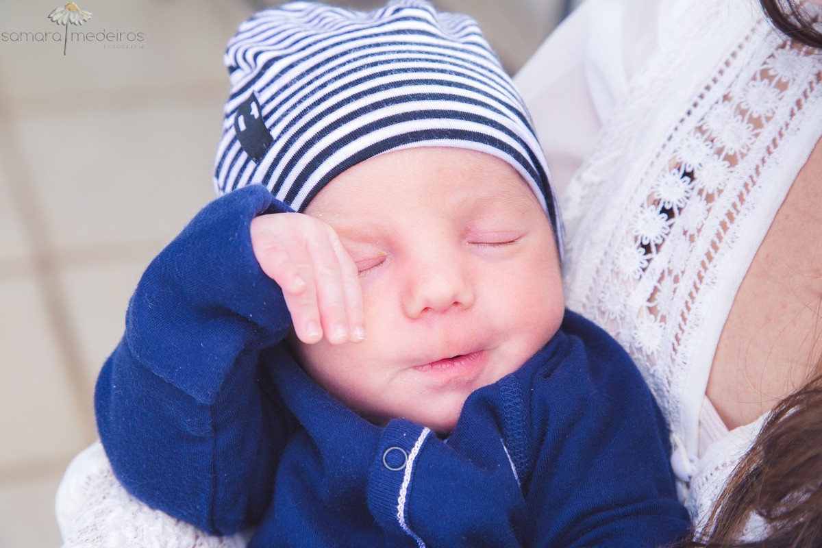 Bebê recém nascido coçando o olhinho de sono, durante sessão de fotos natural em casa.