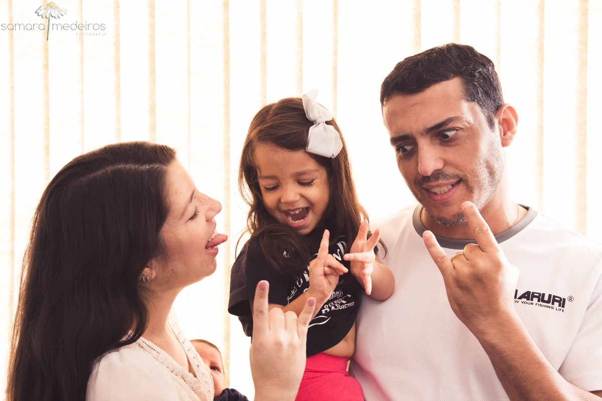 Mãe, pai e criança se divertindo fazendo caretas durante sessão de fotos de família, em sua própria casa.