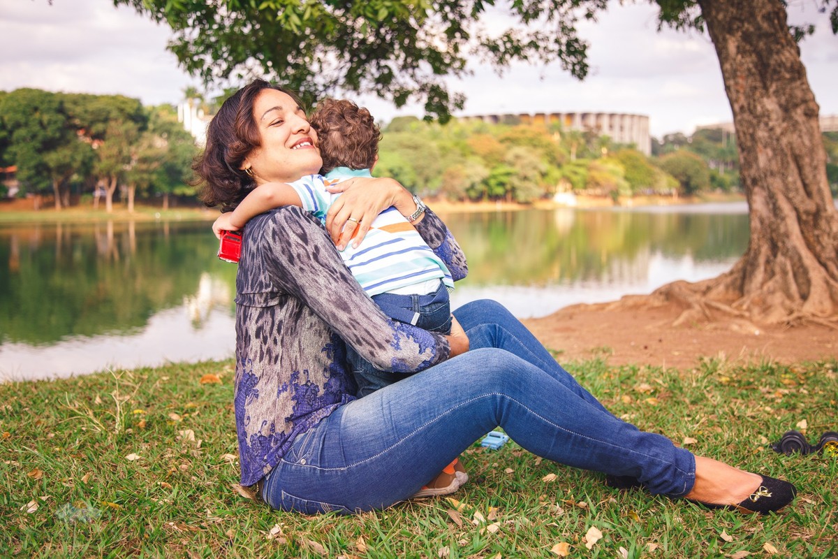 Mãe e filho se abraçando, sentados na grama, com o Mineirão, famoso ponto turístico de Belo Horizonte, ao fundo da foto.