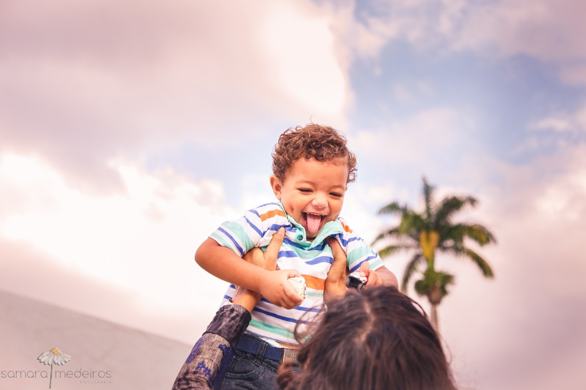Mãe brincando de jogar o filho, que gargalha, para cima, durante sessão de fotos em Belo Horizonte.