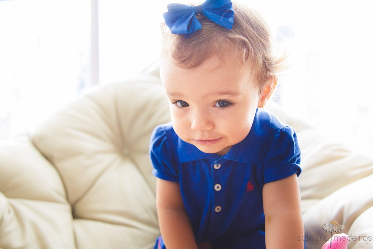 Criança sentada em uma poltrona, olhando para a câmera e fazendo uma careta.