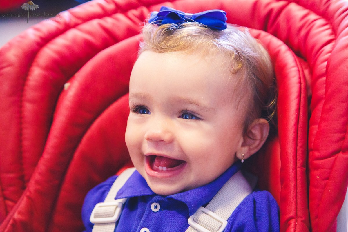 Criança sentada em sua cadeirinha de comer, aguardando o almoço, sorrindo.