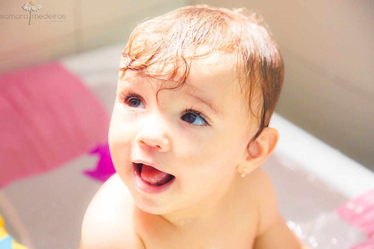 Criança tomando banho, olhando para cima e sorrindo para algo que a distraiu, durante sessão de fotos infantil, em Belo Horizonte.