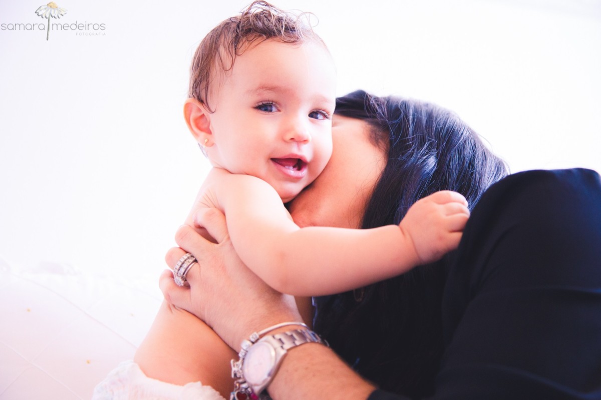 Criança ganhando um beijo de sua mãe, em sessão de fotos de família, olhando para a câmera e sorrindo.
