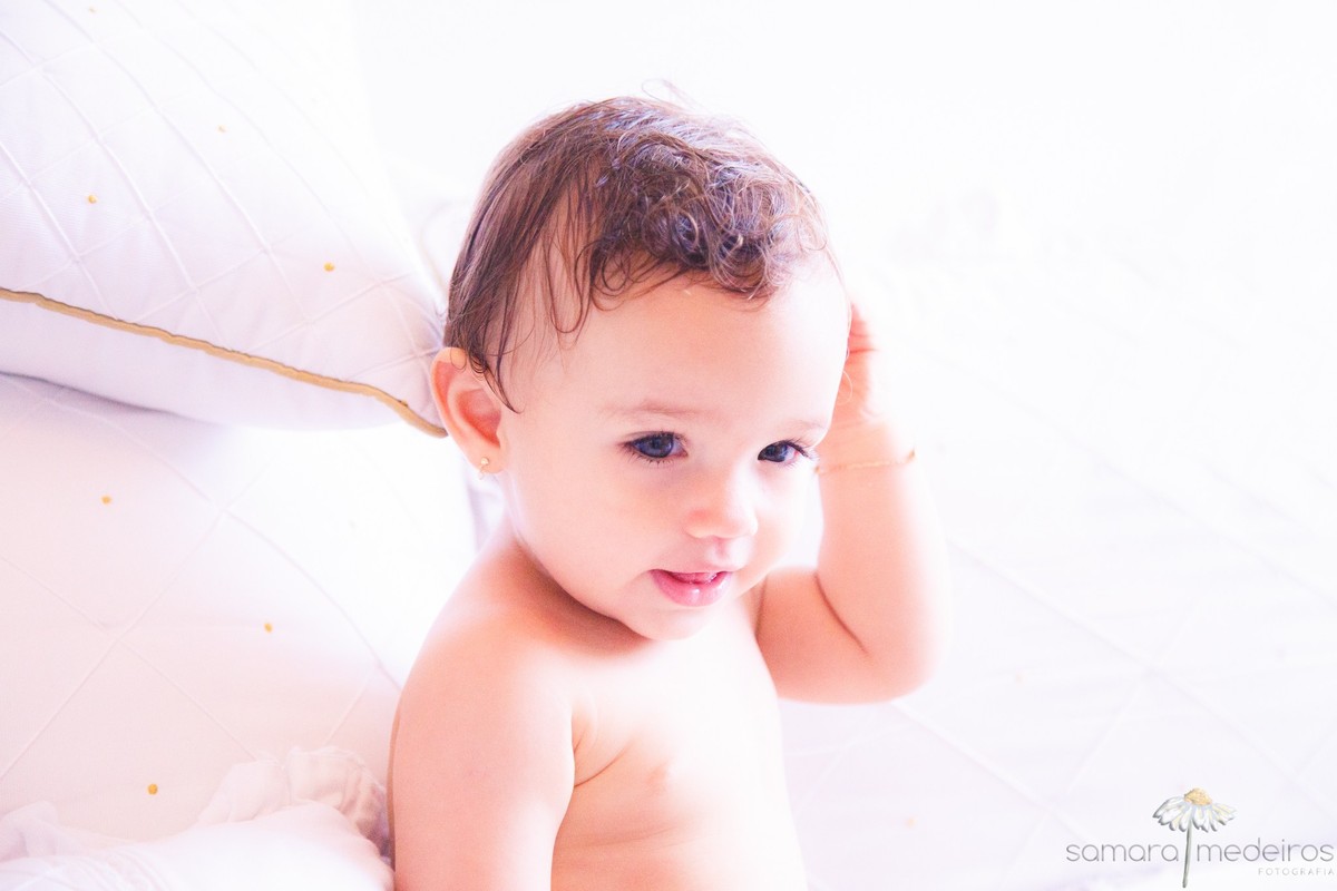 Criança após o banho, durante sessão fotográfica infantil, sentada em sua cama, olhando distraída para o lado.